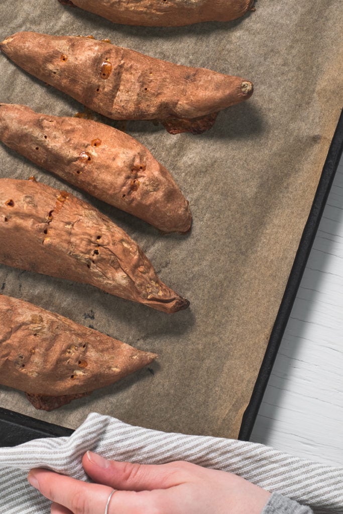 A pan of freshly baked sweet potato halves, oozing with juices.