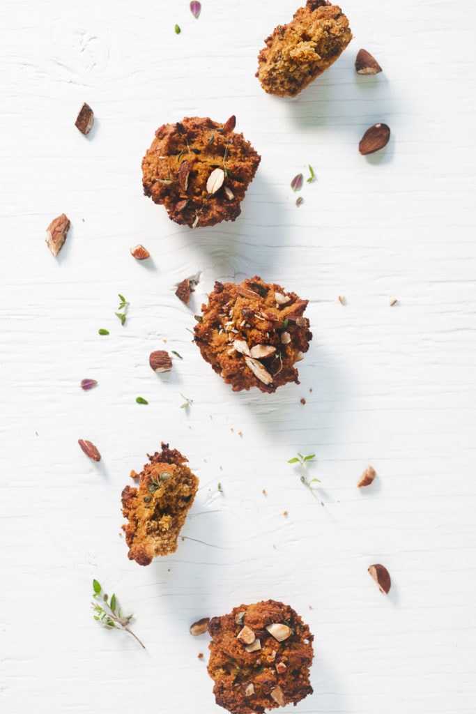 Sweet Potato Muffins laying in a staggered row sprinkled with toasted almonds, thyme and surrounded by crumbs.