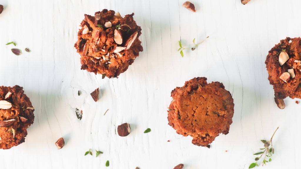 Four Sweet Potato Muffins staggered in a row with toasted almonds and thyme sprinkled on top.