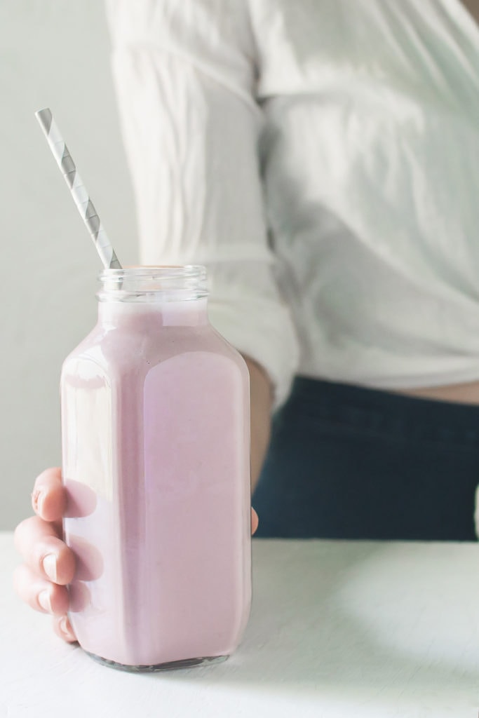 A person grabbing a freshly poured, pink strawberry smoothie.