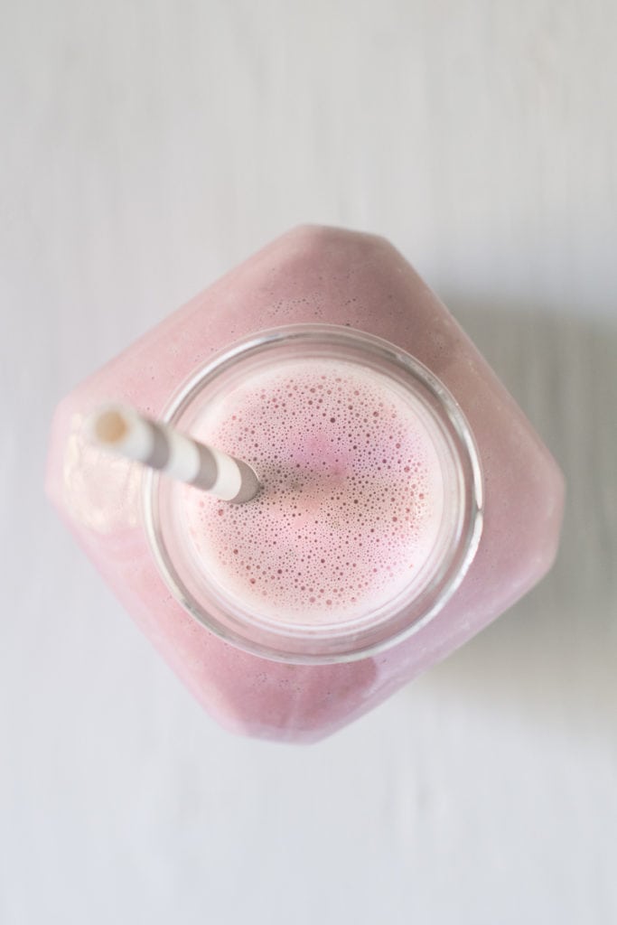 The top of a frothy, pink strawberry smoothie freshly poured into a bottle with a straw.