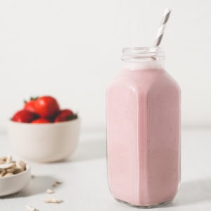 A healthy strawberry Shortcake Smoothie next to spilled raw cashews and a bowl of strawberries.