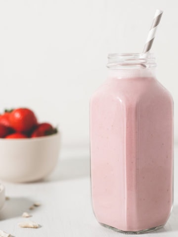 A healthy strawberry Shortcake Smoothie next to spilled raw cashews and a bowl of strawberries.