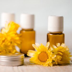 Yellow Calendula flowers sitting in front of essential oil bottles and beside a metal tin.