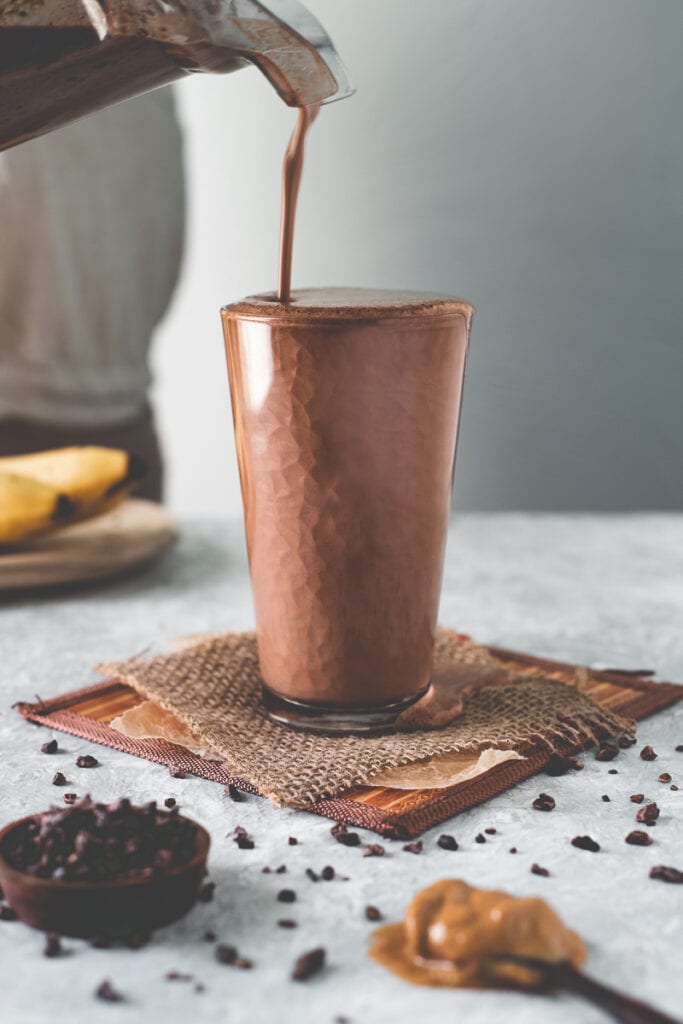 A dark chocolate smoothie being poured into a brimming glass.