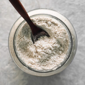 A wooden spoon sunken into a jar of fluffy oat flour.