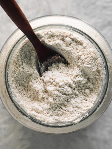 A wooden spoon sunken into a jar of fluffy oat flour.