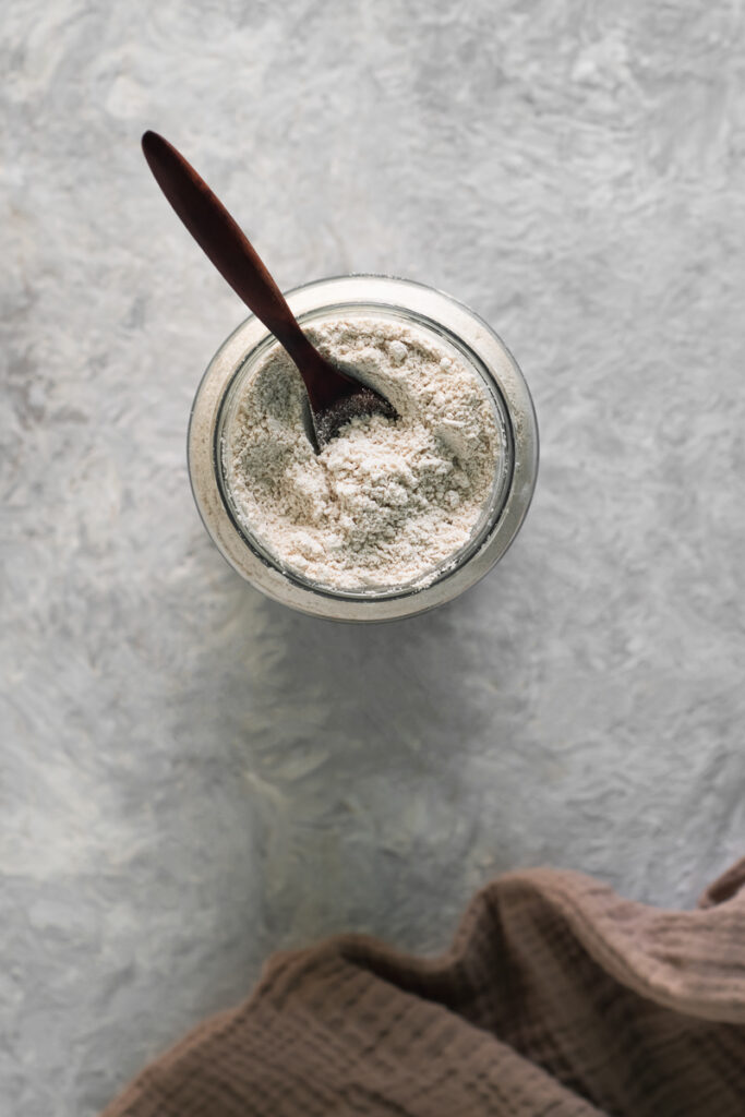 The top of an open jar filled with oat flour and a submerged wooden spoon.