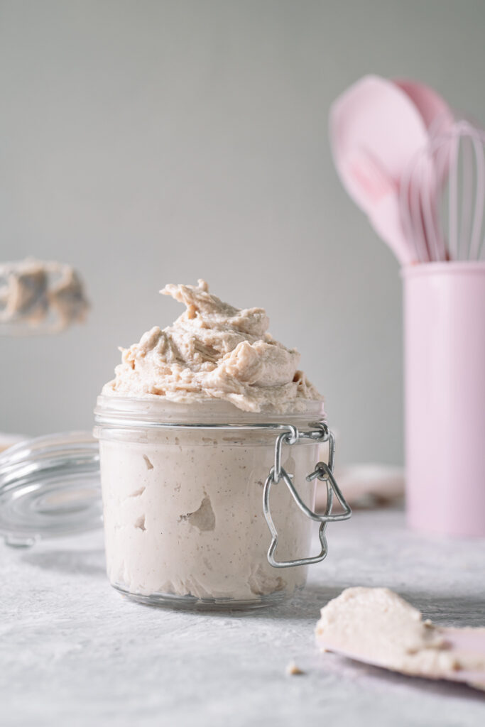 Homemade whipped cream swirled in an open latch jar with freshly used beaters of a hand mixer and a container of pink baking utensils behind.