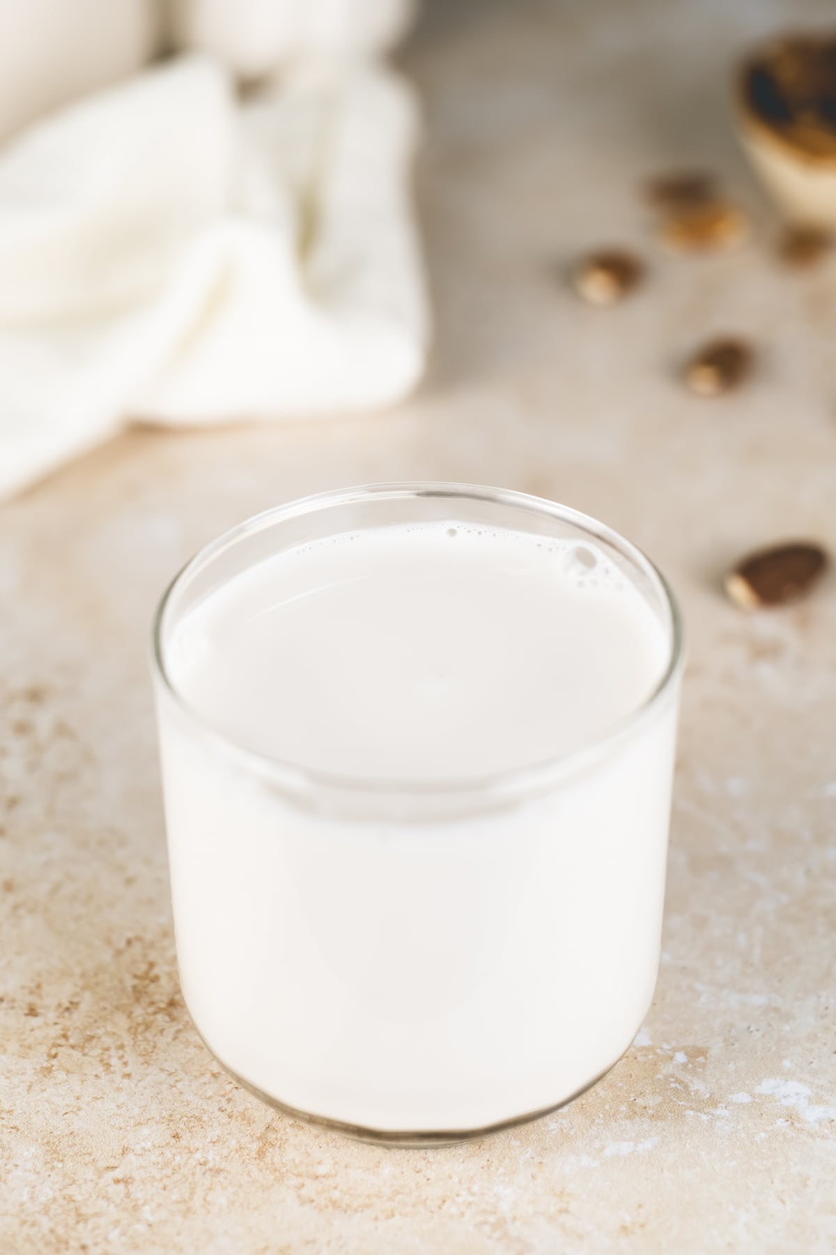 A full glass of milk in front of spilt raw almonds and white linen cloth.