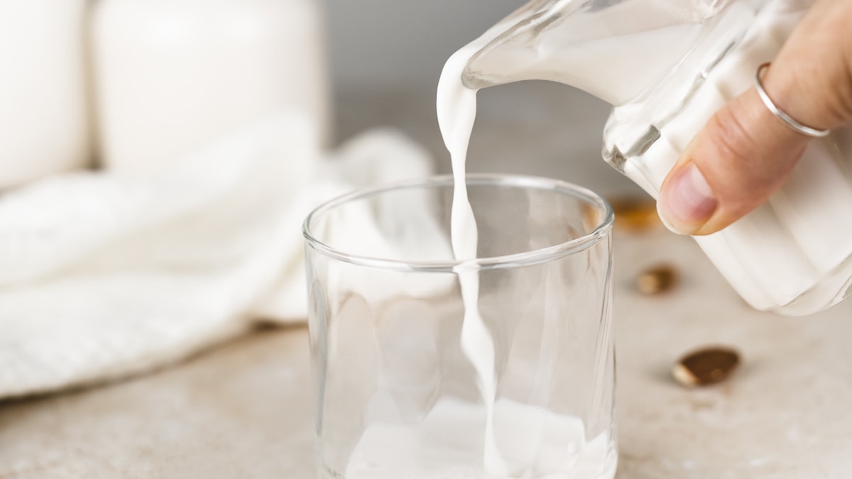 Fresh almond milk being poured from a creamer jug into a glass.