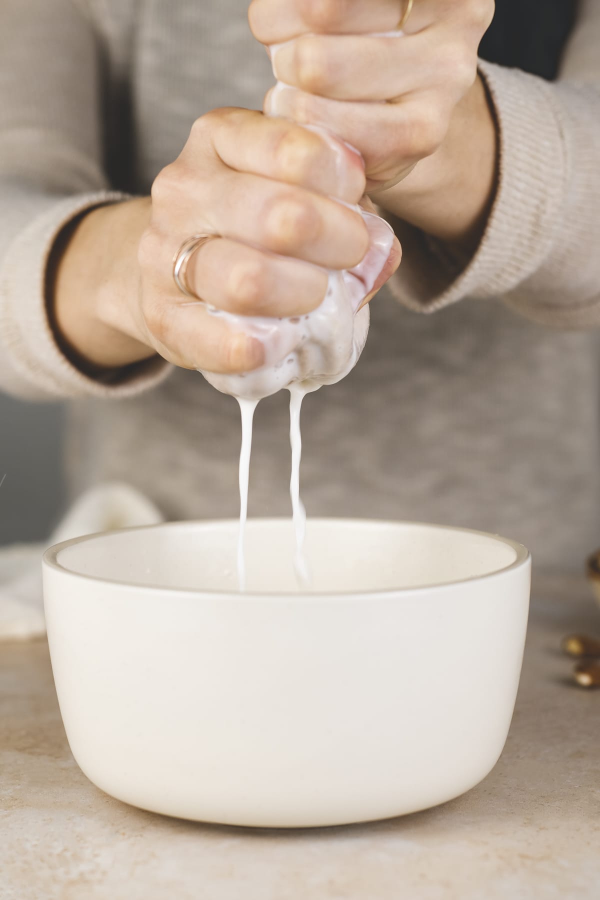 Almond Milk being squeezed through a nut milk bag into a bowl.