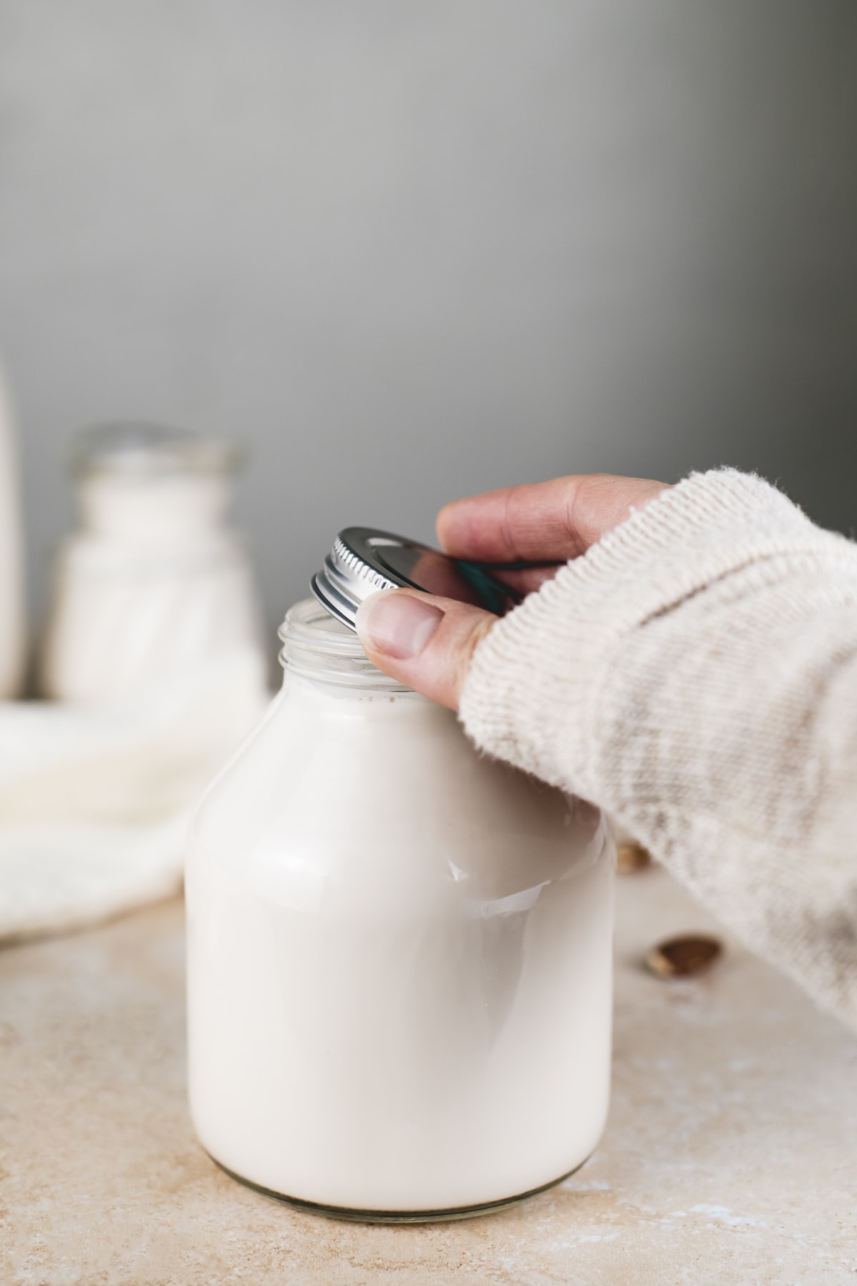 A lid being placed on a jar full of homemade almond milk.