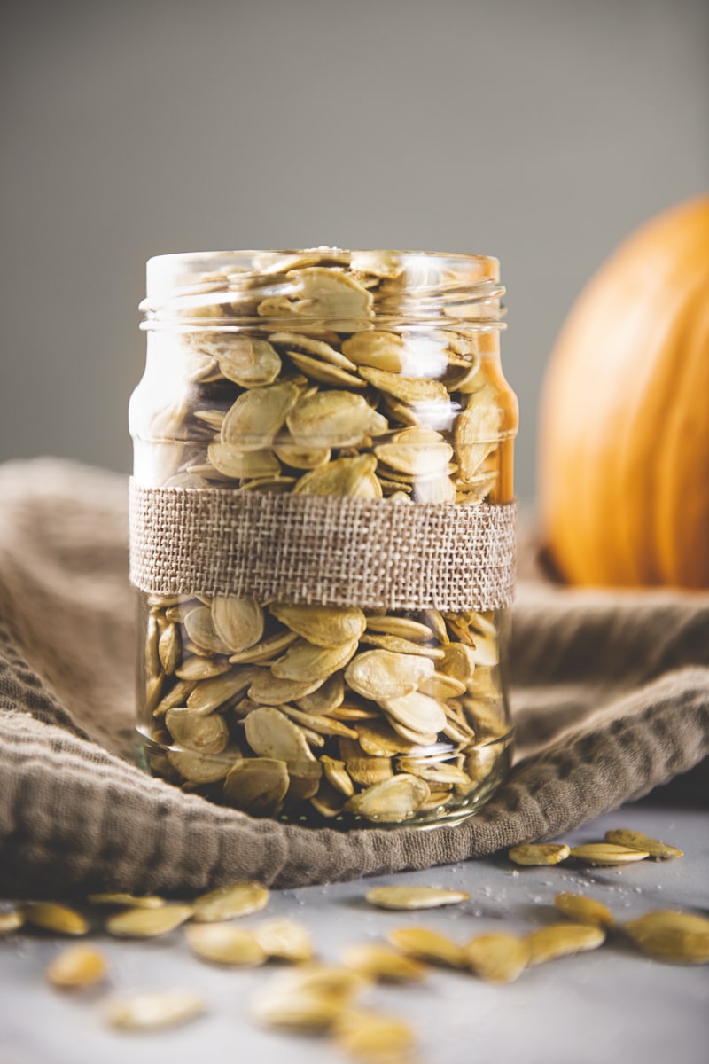 A jar full of roasted pumpkin seeds beside a fresh pumpkin. 