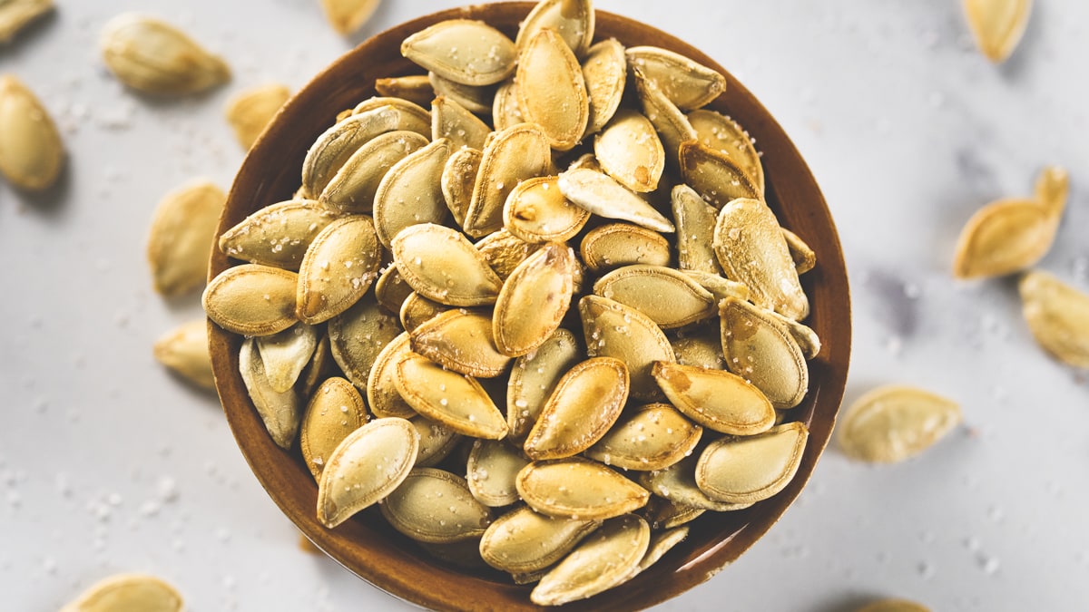 An overflowing bowl of baked golden-brown pumpkin seeds.