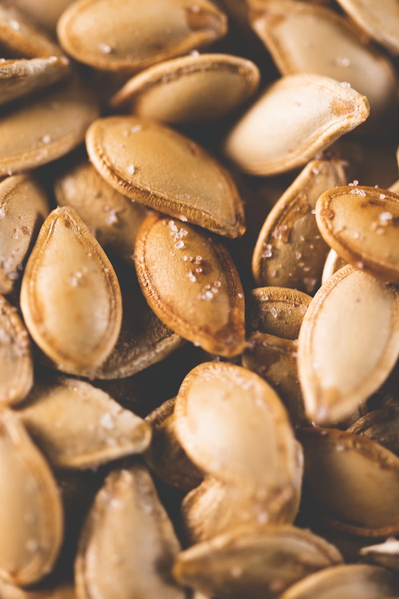 A pile of golden-brown pumpkin seeds lightly dusted with pink Himalayan salt.