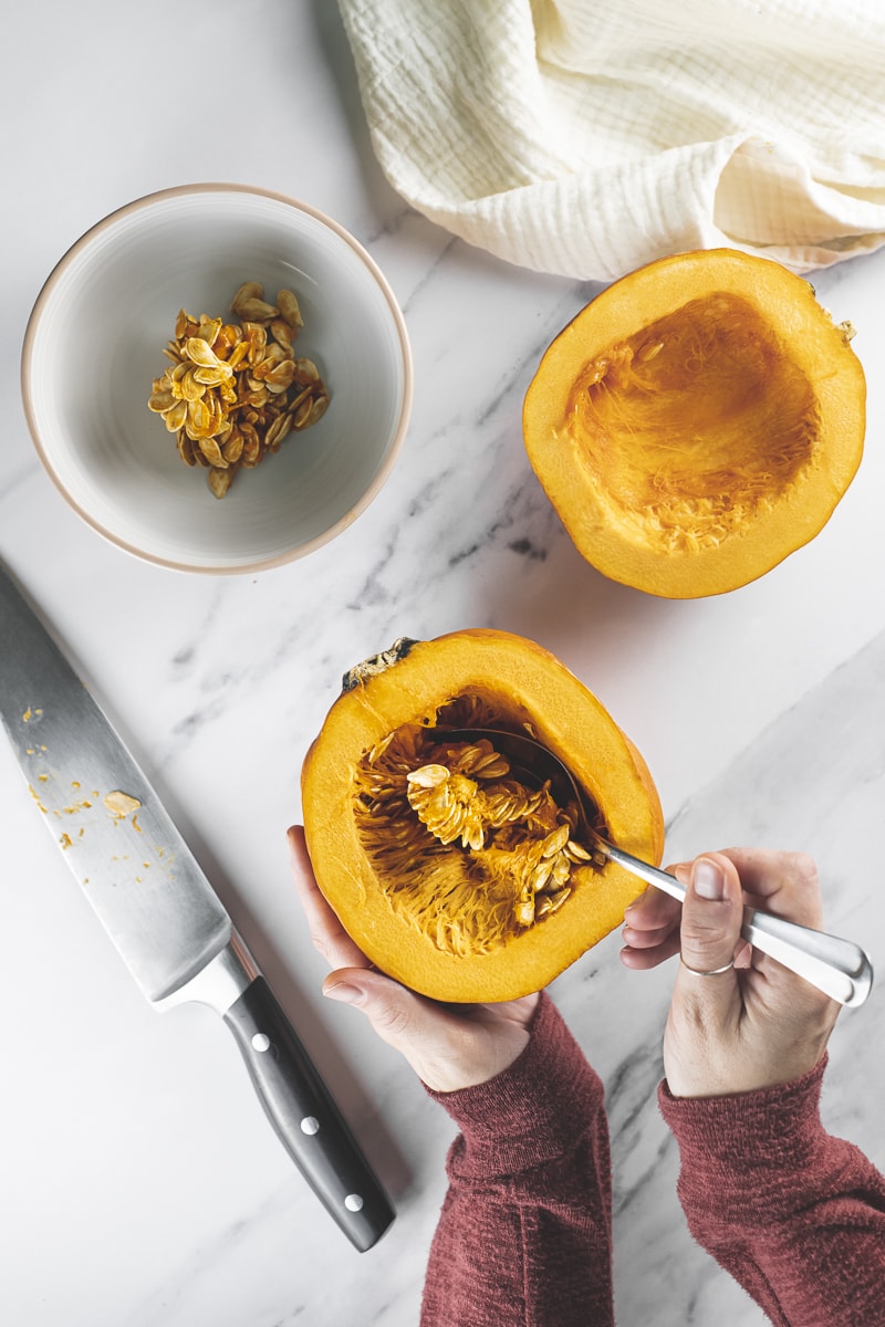 Pumpkin seeds being scooped out of a halved pumpkin into a bowl.