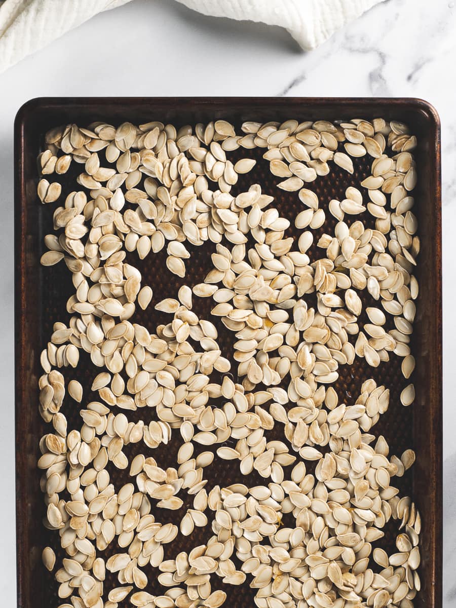 Raw pumpkin seeds spread evenly on a baking sheet.