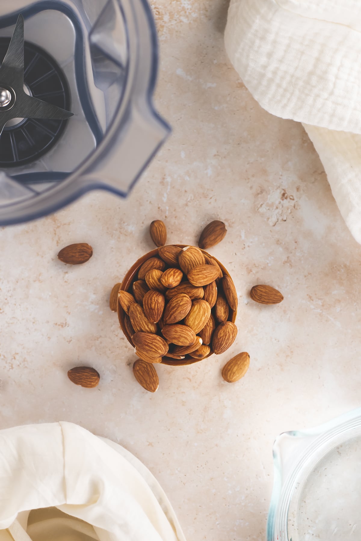 An overflowing bowl of almonds surrounded by a blender jug, bowl and nut milk bag.