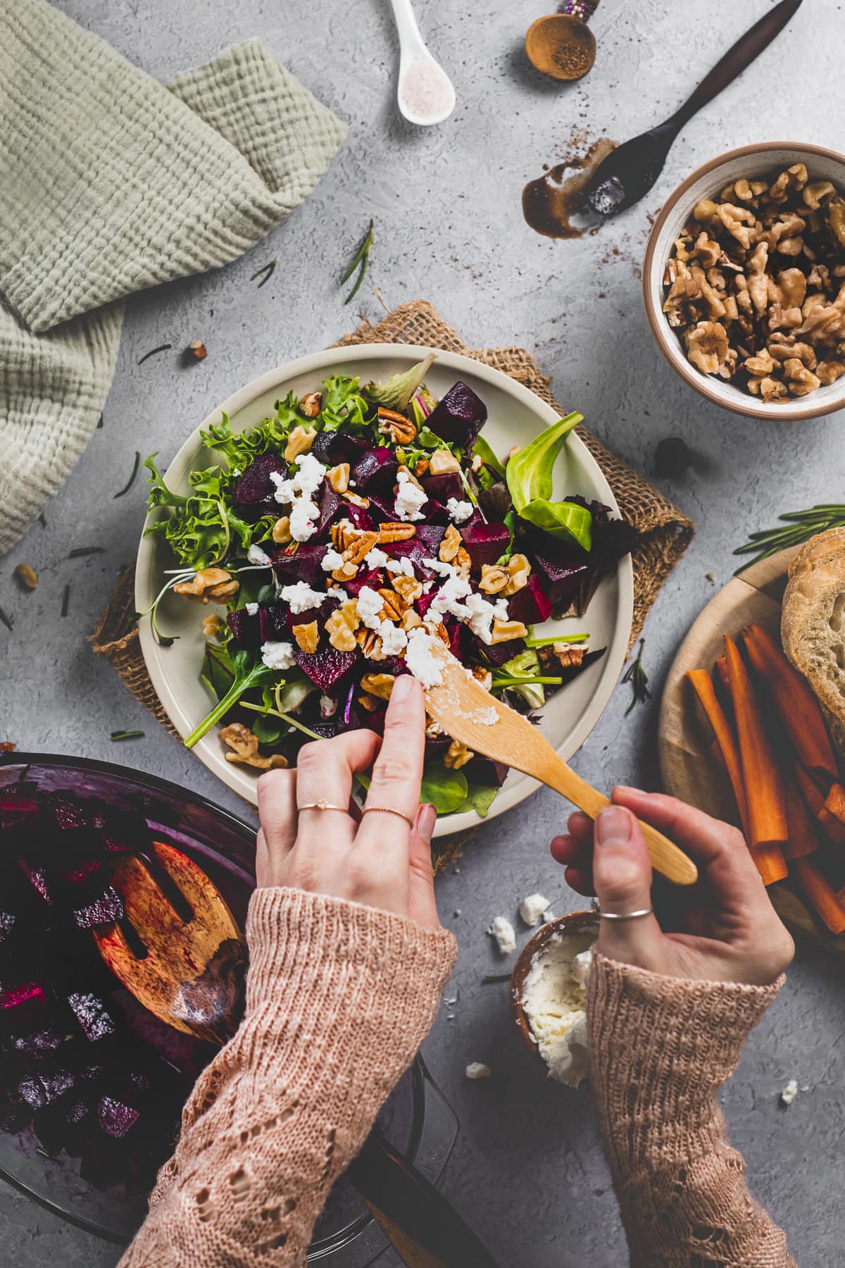 A salad with roasted beets being topped with walnuts, pecans and goat cheese.