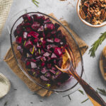A wooden serving spoon resting in a roasting dish full of baked balsamic glazed beets topped with fresh rosemary.