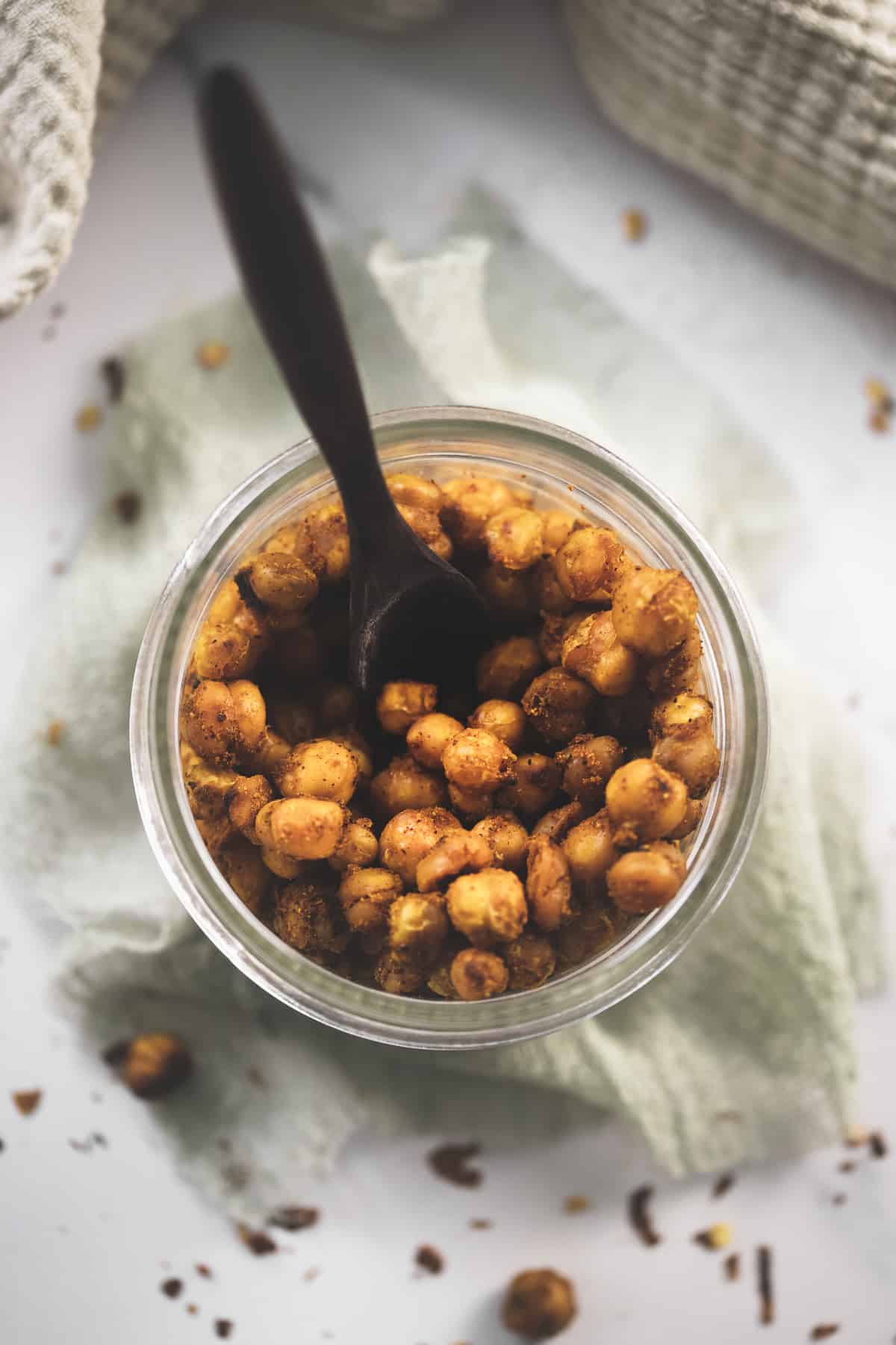 A jar of seasoned, roasted chickpeas in a jar with a wooden serving spoon.