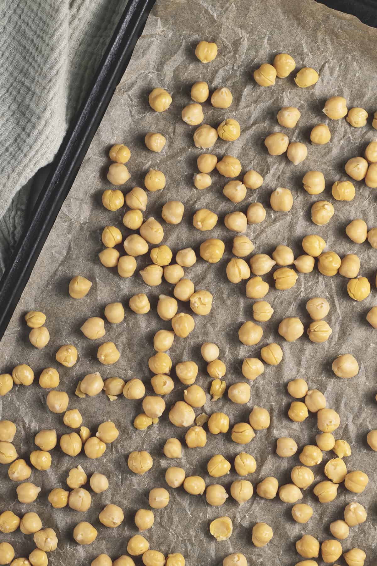 Unseasoned chickpeas spread evenly on a baking sheet lined with unbleached parchment paper and a sage cloth beside.
