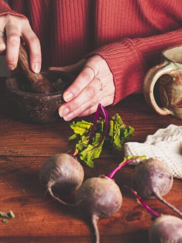 Healing herbs being prepared in a mortar and pestle on a rustic table with beetroot and dried sage.