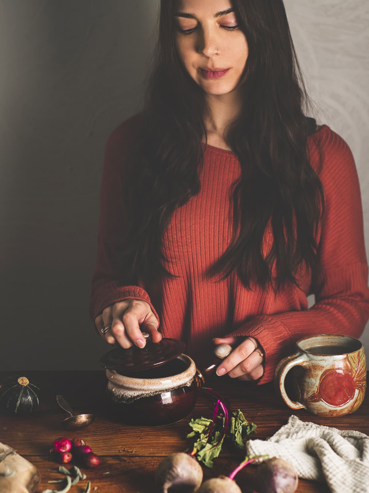 A dark-haired woman preparing whole foods on a rustic table with fresh beets and beet greens.