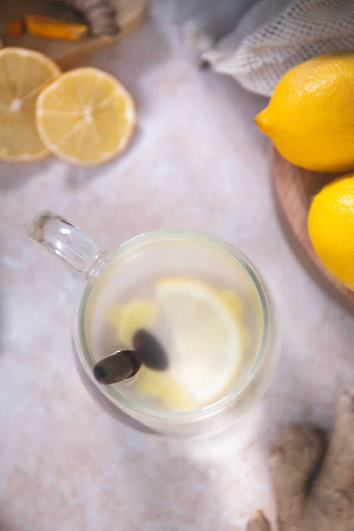 A wooden teaspoon resting in a mug of water with freshly sliced lemon and ginger root.