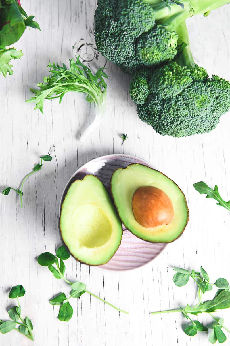 Two avocado halves lying face-up on a pink plate surrounded by fresh greens.