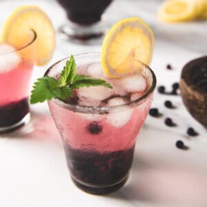 Two glasses of infused blueberry lemon water garnished with lemon slices and a sprig of lemon balm.