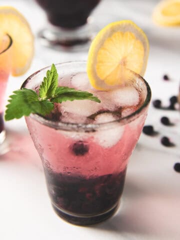 Two glasses of infused blueberry lemon water garnished with lemon slices and a sprig of lemon balm.