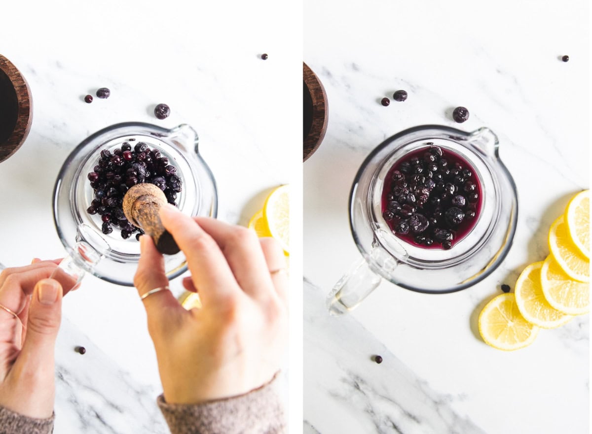 Muddled blueberries in a glass pitcher.