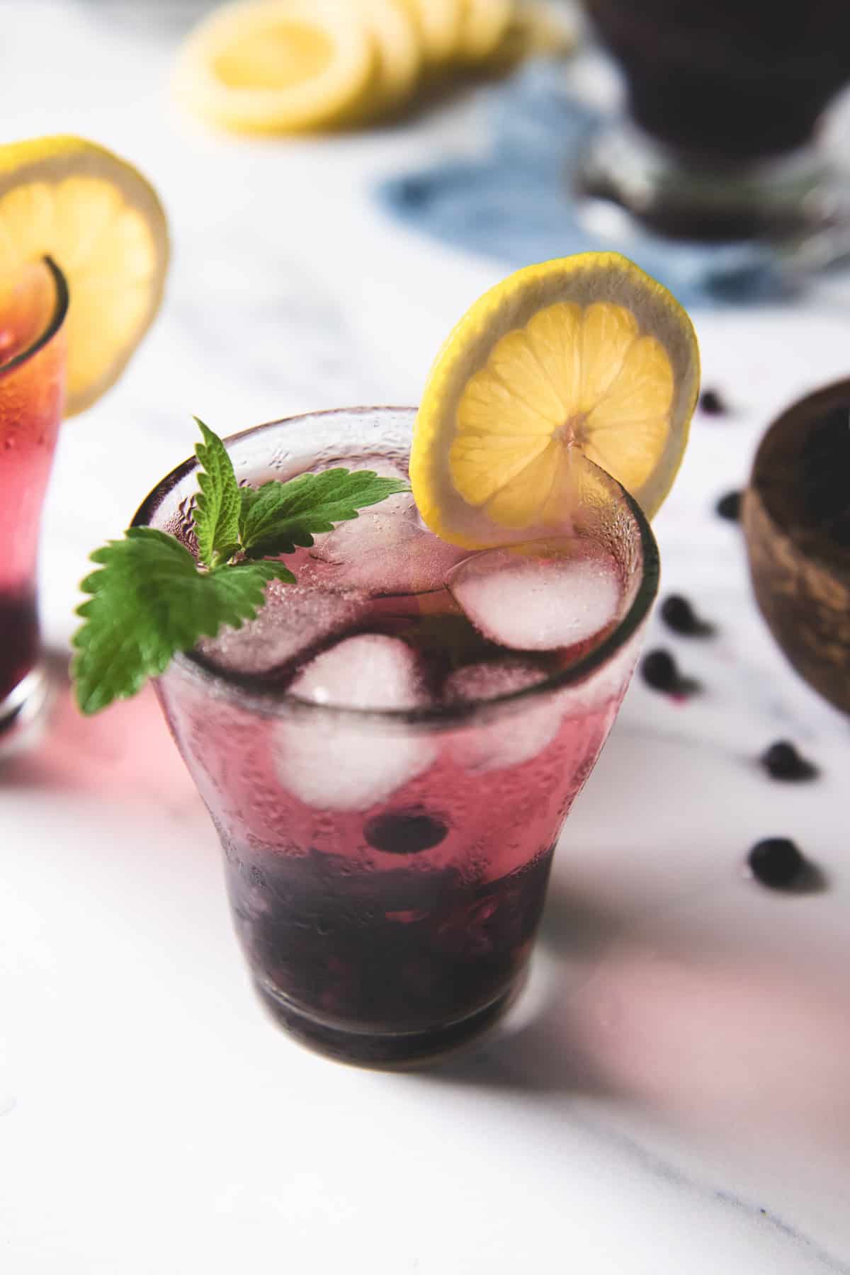 Iced blueberry lemon water in a glass garnished with a lemon slice and fresh lemon balm.
