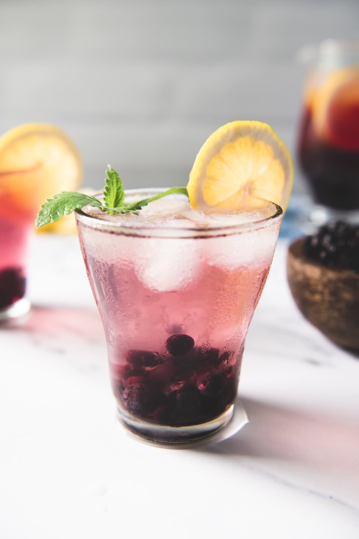 Two glasses of infused water with blueberries and lemon slices, garnished with a sprig of lemon balm.