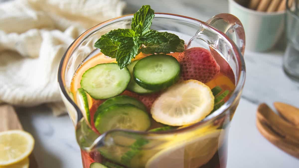 A pitcher filled with water infused with cucumber, lemon, strawberries and mint.