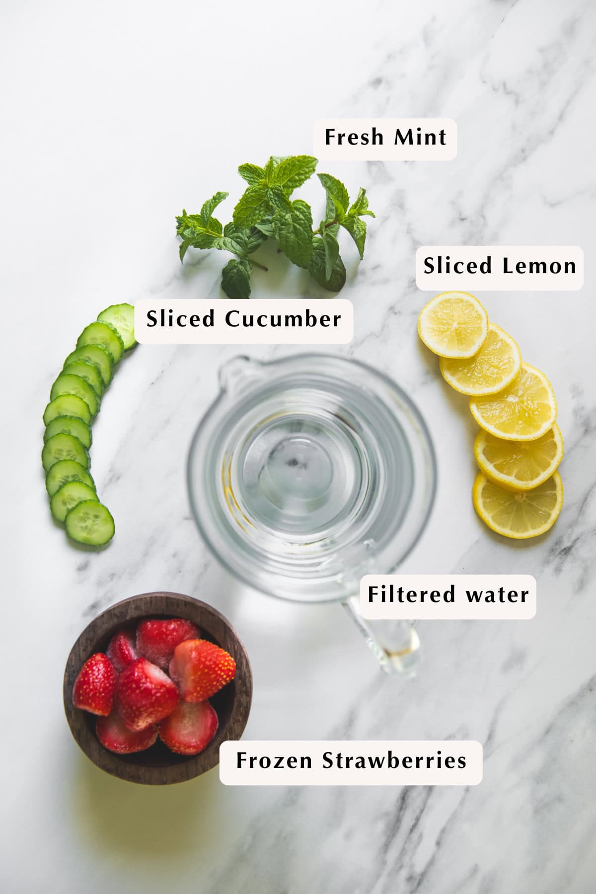 A pitcher of filtered water, fresh mint, frozen strawberries, sliced cucumber and sliced lemon.