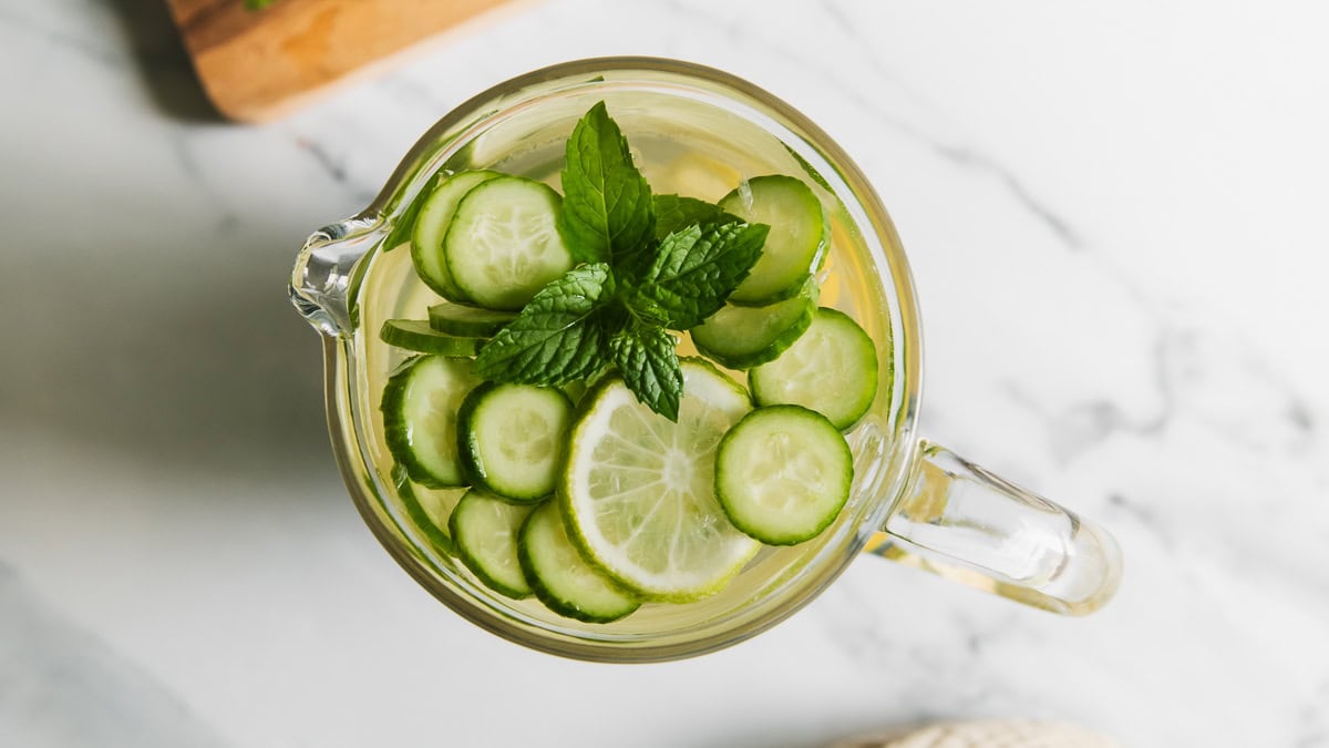 Slices of cucumber and lime floating in a pitcher of water with a sprig of mint.