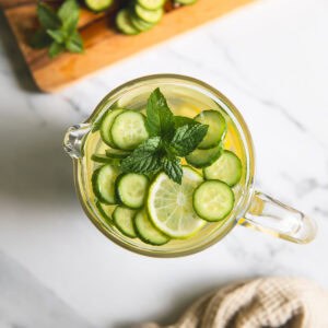 Slices of cucumber and lime floating in a pitcher of water with a sprig of mint.