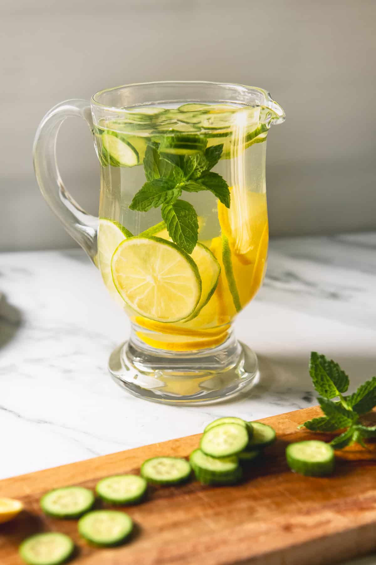 A sprig of mint with sliced lemon, lime and cucumber infusing in a pitcher of water.