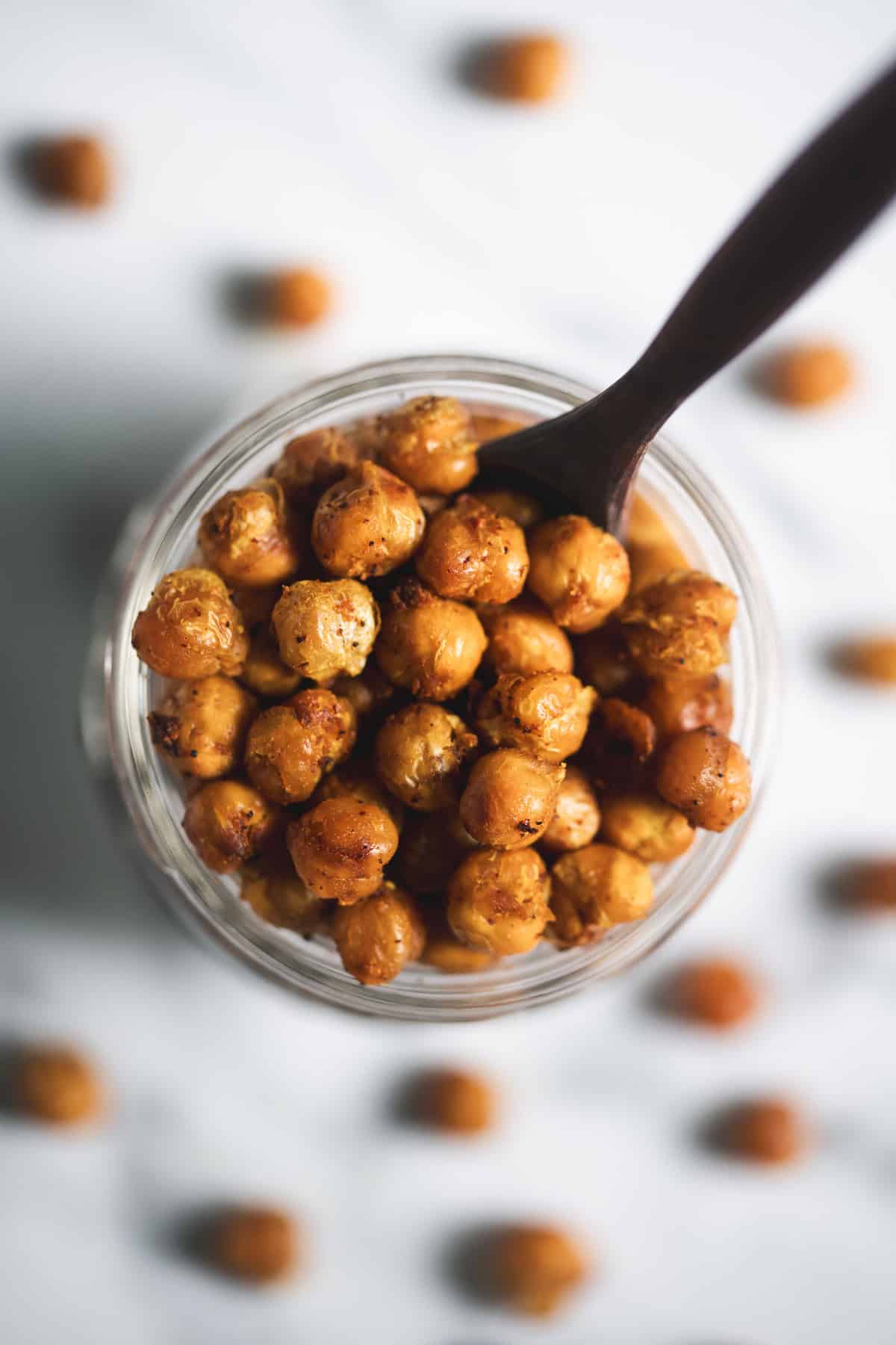 An overflowing jar of roasted chickpeas with a small wooden serving spoon.