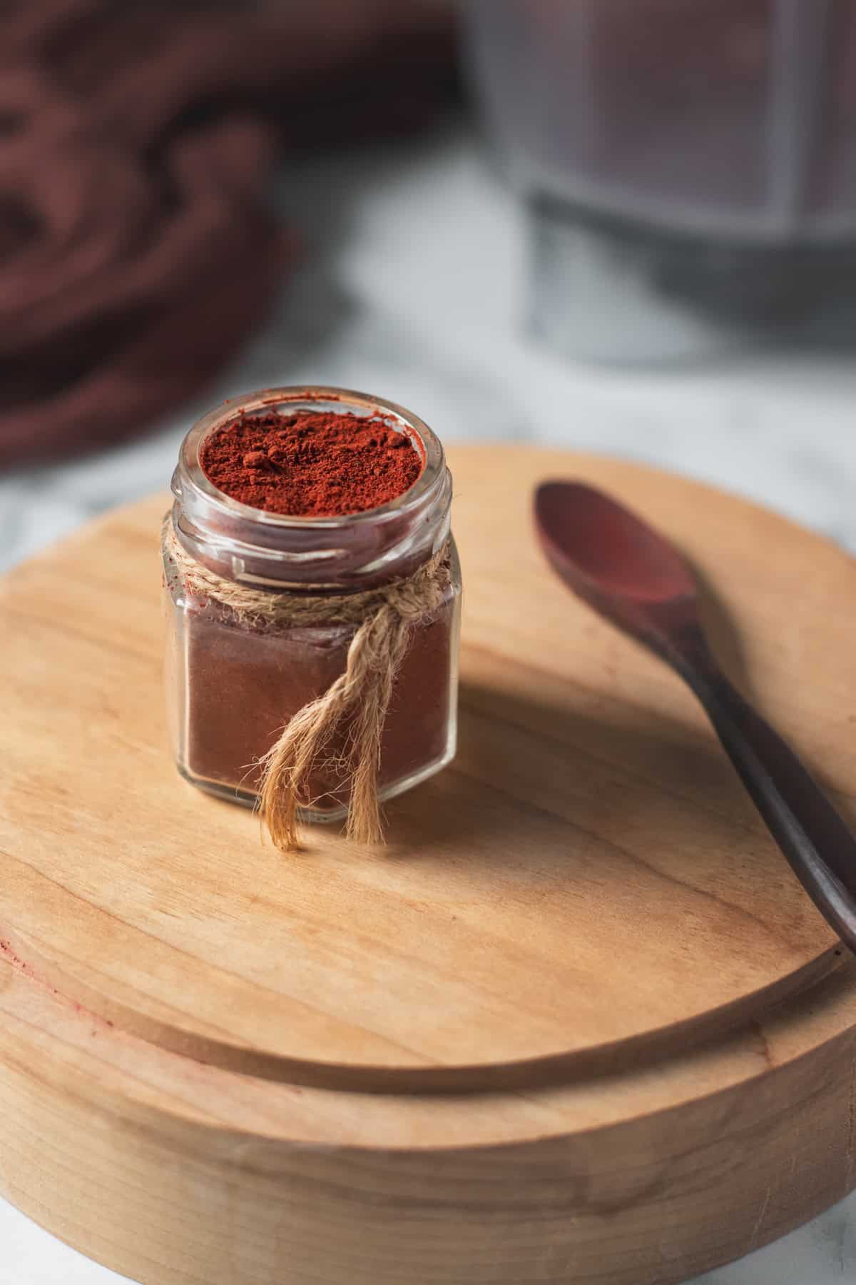 A Jar of beetroot powder beside a wooden spoon and a blender jug.