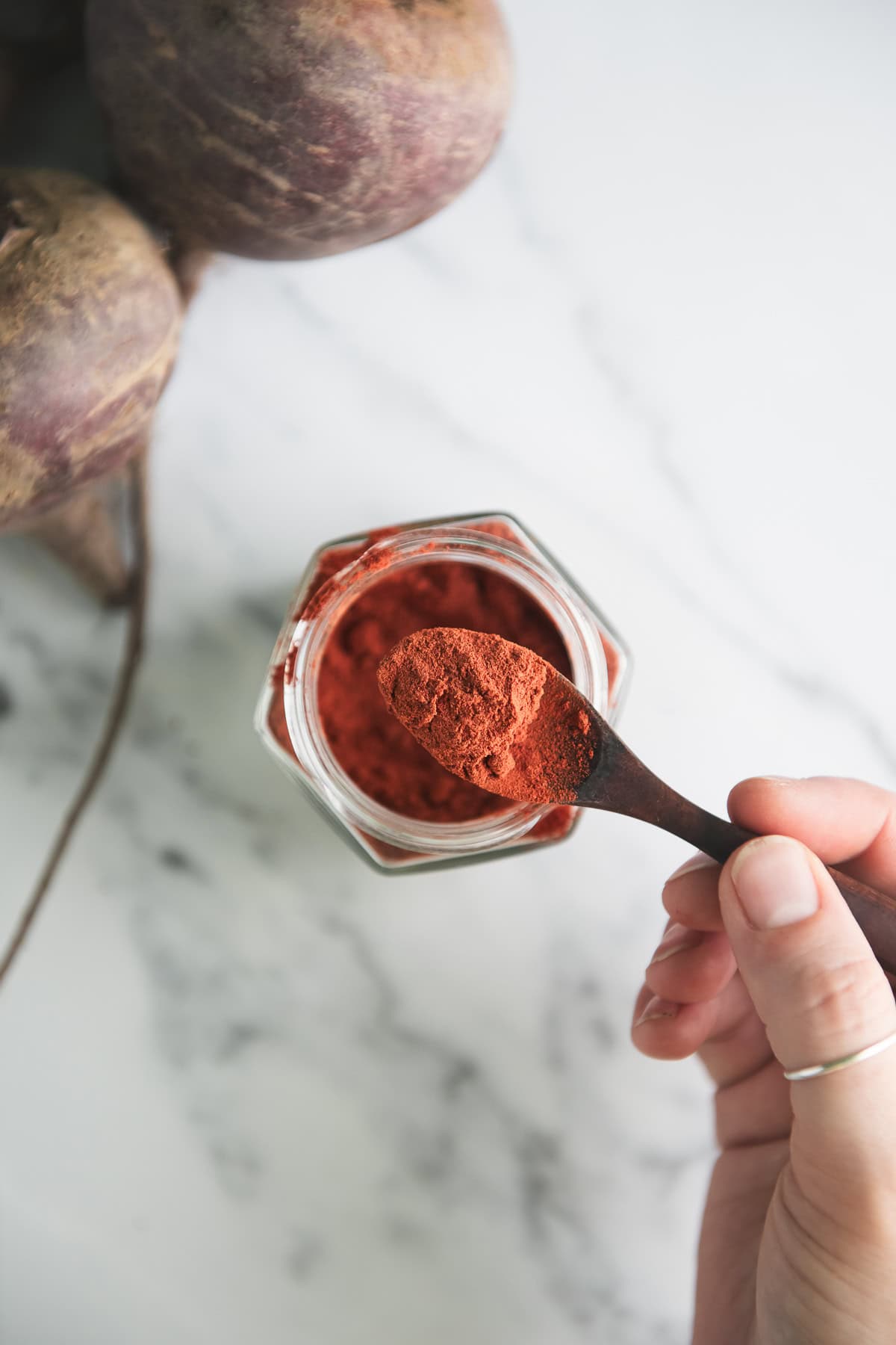 A spoonful of beetroot powder being lifted out of a jar.