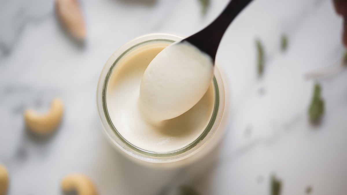 A spoonful of creamy cashew sauce dripping into a jar.