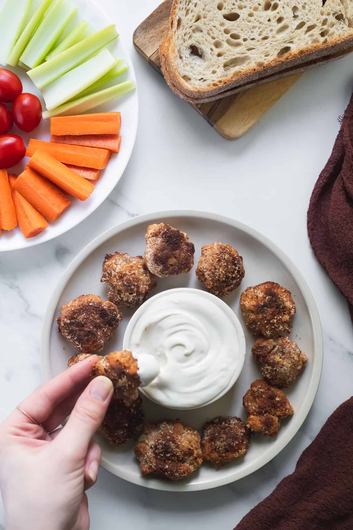 A chicken nugget dipped in a bowl of creamy cashew garlic sauce beside a platter of vegetables.