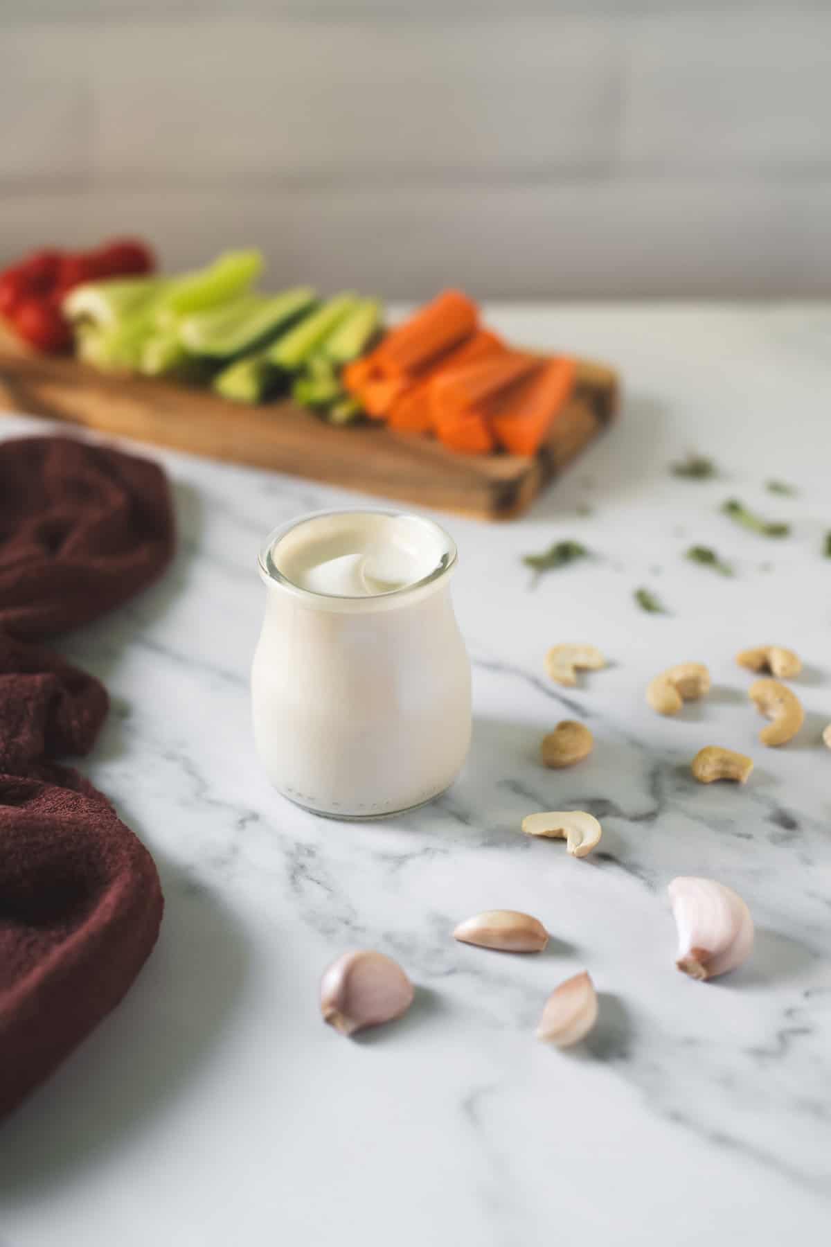 Creamy cashew garlic dip swirled in a glass jar beside a veggie platter.