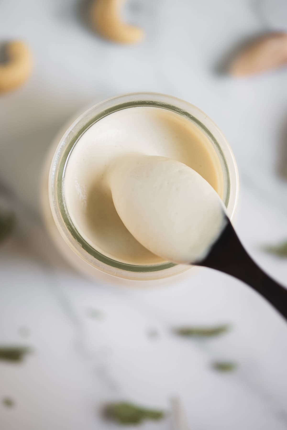 A spoonful of creamy cashew sauce dripping into a jar.