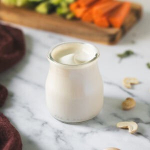 Creamy cashew garlic dip swirled in a glass jar beside a veggie platter.