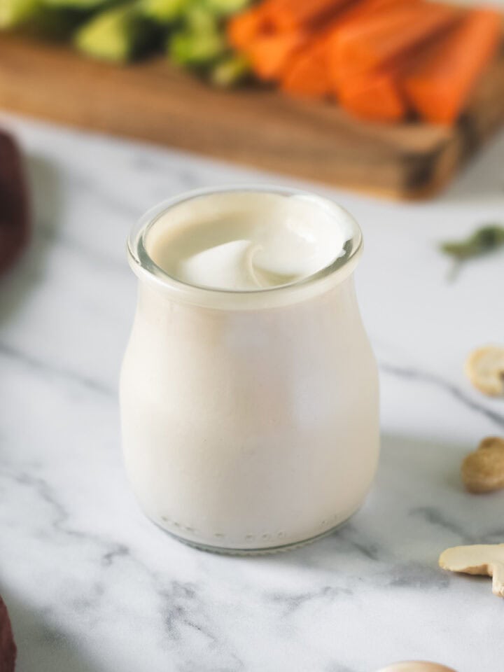 Creamy cashew garlic dip swirled in a glass jar beside a veggie platter.